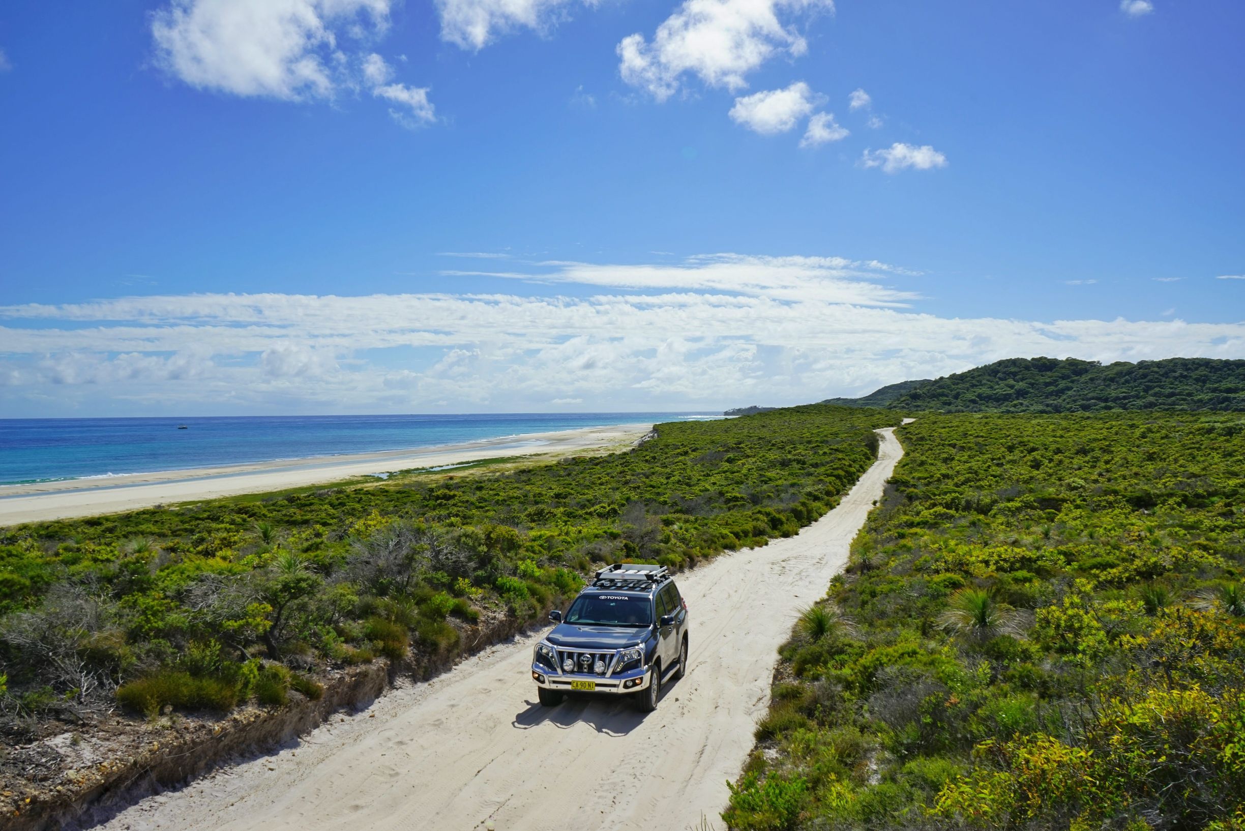 Car driving through bushland on sandy track